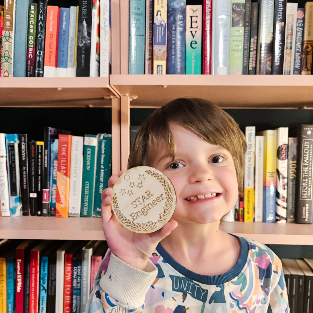 Brontë stands in front of a bookcase. She is smiling and holding a wood medal that is engraved with the words, STAR Engineer.